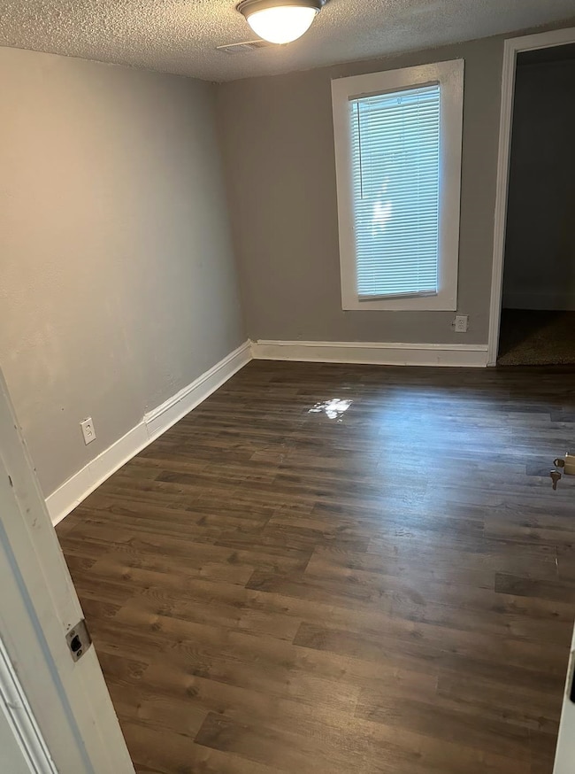 Empty room with dark wood-type flooring and a textured ceiling