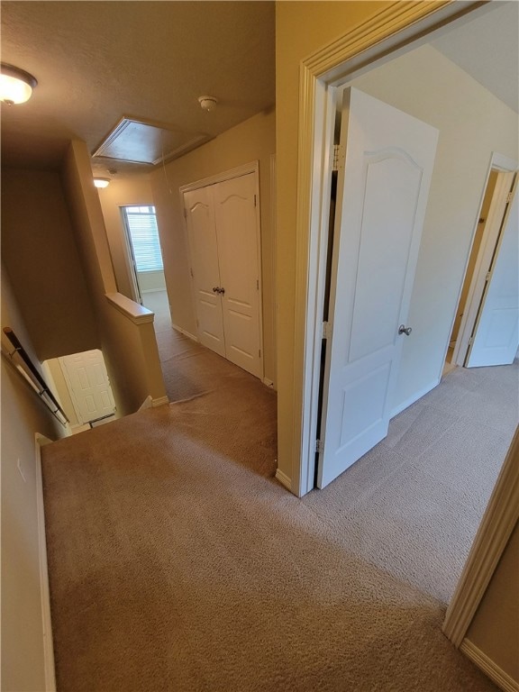 Corridor with an upstairs landing, attic access, and light carpet