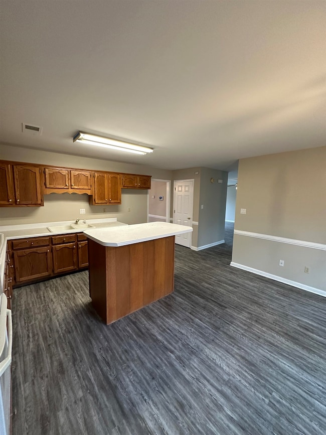 Kitchen featuring dark wood-style flooring, light countertops, a center island, and brown cabinetry