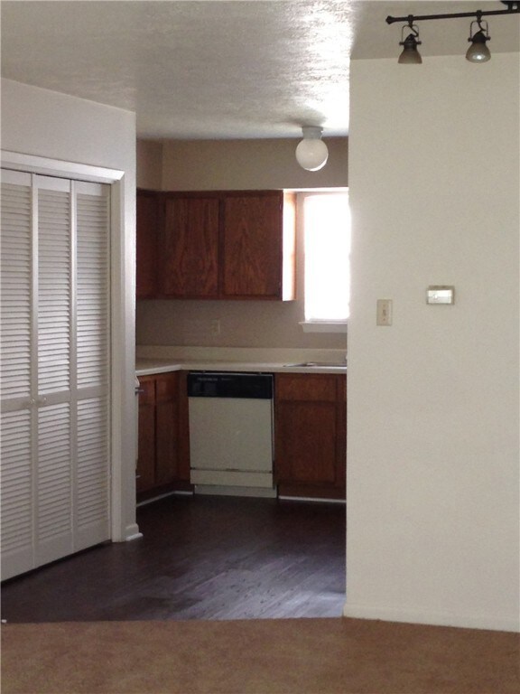 Kitchen with light countertops, dark wood-type flooring, brown cabinetry, and white dishwasher