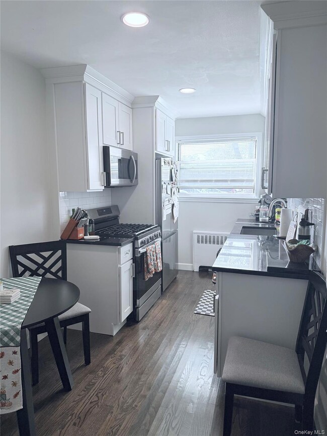 Kitchen featuring appliances with stainless steel finishes, tasteful backsplash, dark countertops, dark wood-type flooring, and white cabinets