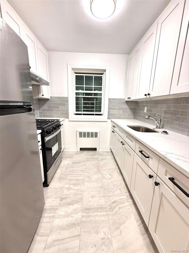 Kitchen featuring appliances with stainless steel finishes, white cabinets, light stone countertops, and radiator heating unit