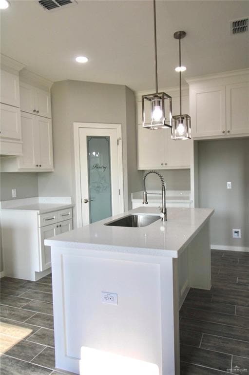 Kitchen with a sink, recessed lighting, wood tiled floors, a center island with sink, and white cabinets