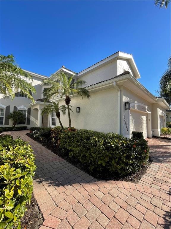 Paved walkway to front door. Side view also shows property featuring stucco siding, a garage, driveway, new paint and lighting.
