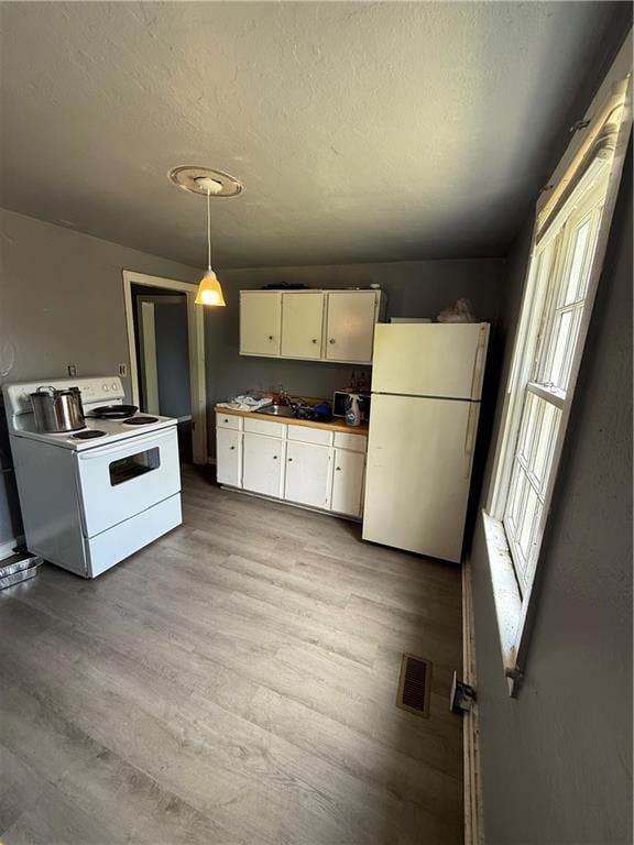 Kitchen featuring fridge, range, white cabinets, light wood finished floors, and a textured ceiling