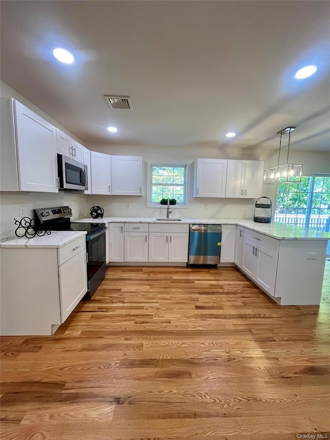 Kitchen featuring white cabinets, a peninsula, appliances with stainless steel finishes, light wood-style flooring, and pendant lighting