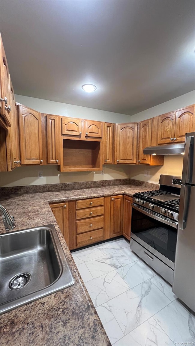 Kitchen with stainless steel appliances, brown cabinets, dark countertops, and light marble finish floors