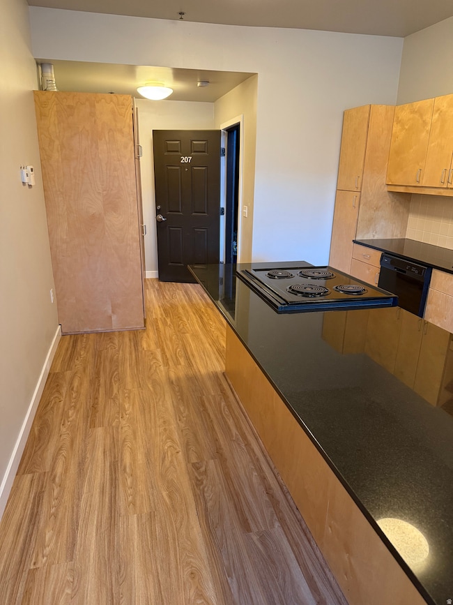 Kitchen with light wood finished floors, light brown cabinets, black appliances, and dark stone counters