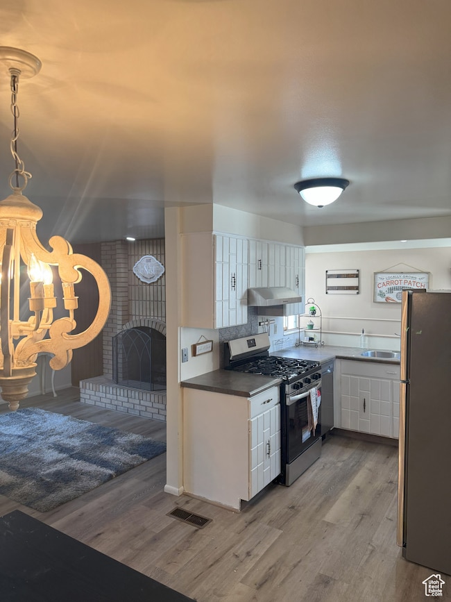 Kitchen featuring white cabinetry, appliances with stainless steel finishes, light wood finished floors, under cabinet range hood, and a fireplace