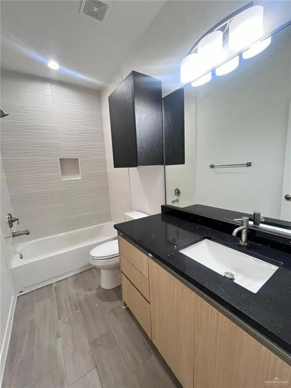 Full bathroom featuring hardwood / wood-style floors, vanity, toilet, and tiled shower / bath combo