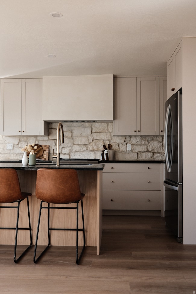 Kitchen featuring a kitchen bar, freestanding refrigerator, decorative backsplash, and dark wood-style floors