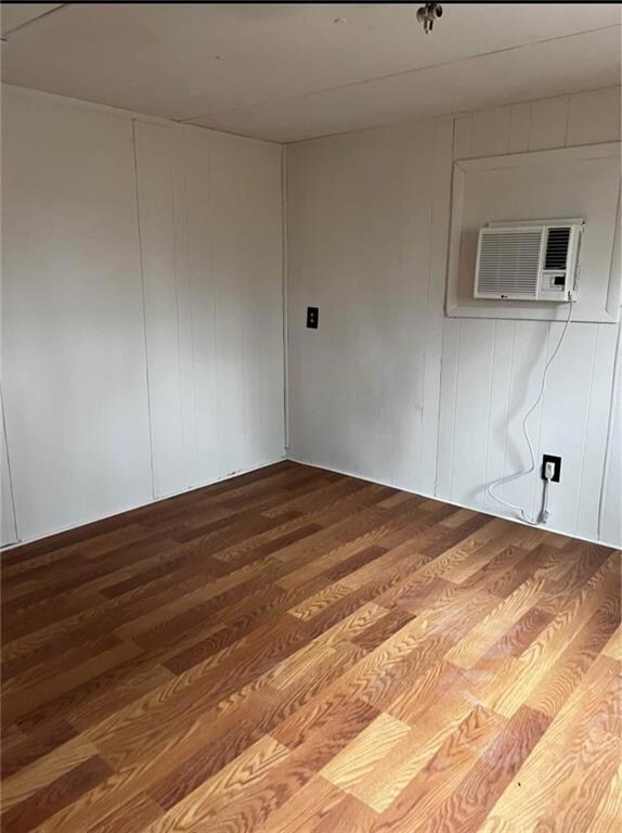 Empty room with wood finished floors, a wall mounted air conditioner, and wood walls