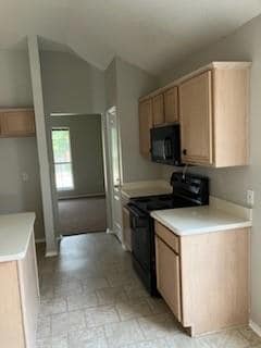 Kitchen with lofted ceiling, black appliances, and light tile floors