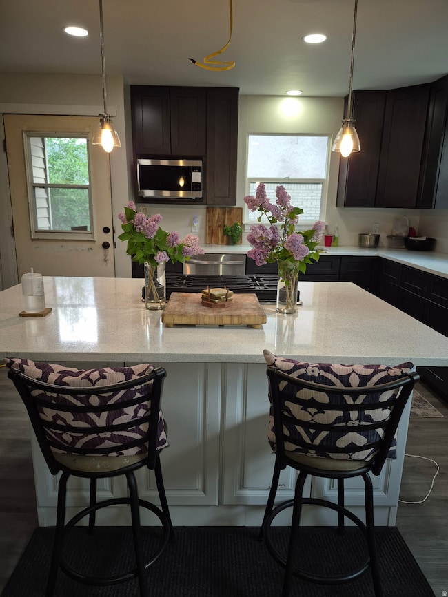 Kitchen with a breakfast bar area, pendant lighting, an island with sink, appliances with stainless steel finishes, and light stone countertops