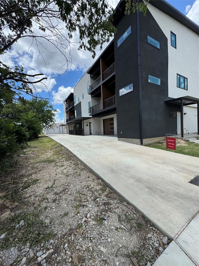 Modern multi-story building with a sleek black and white exterior, featuring balconies and a long driveway. Surrounded by greenery, it offers a contemporary urban living space.