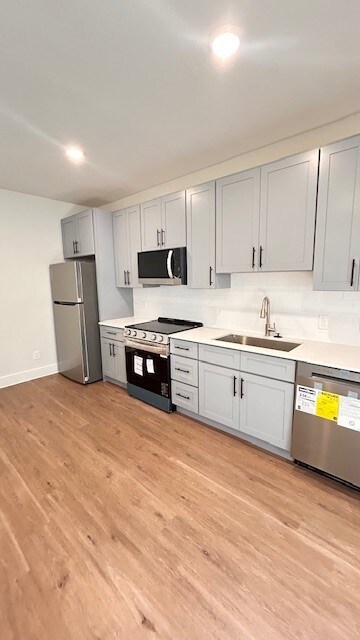 Kitchen featuring stainless steel appliances, light wood-style floors, decorative backsplash, gray cabinets, and recessed lighting