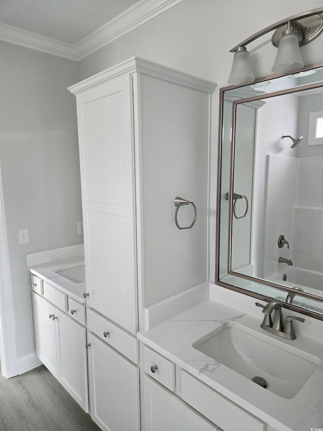 Bathroom with wood finished floors, vanity, ornamental molding, and shower / bathtub combination
