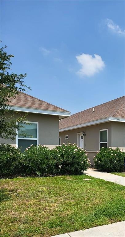View of front facade featuring a front yard, stucco siding, and roof with shingles