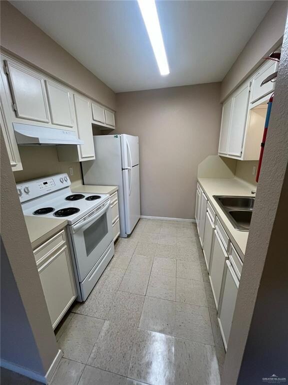 Kitchen with white appliances, under cabinet range hood, light countertops, and a sink