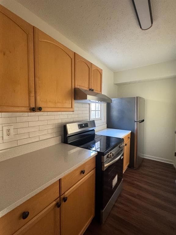 Kitchen featuring stainless steel appliances, dark wood-style flooring, decorative backsplash, light countertops, and a textured ceiling
