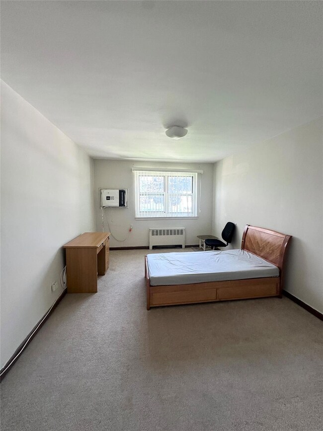 Bedroom with radiator heating unit, carpet floors, and a wall mounted air conditioner