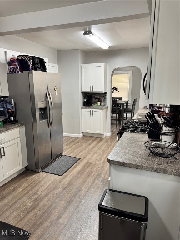 Kitchen with arched walkways, refrigerator, white cabinetry, light wood-style flooring, and tasteful backsplash