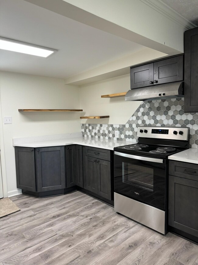 Kitchen with open shelves, stainless steel electric range, under cabinet range hood, light countertops, and tasteful backsplash