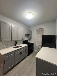 Kitchen featuring black appliances, light countertops, light wood-type flooring, backsplash, and gray cabinetry