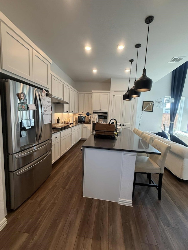 Kitchen with stainless steel appliances, open floor plan, a center island with sink, a kitchen breakfast bar, and decorative light fixtures
