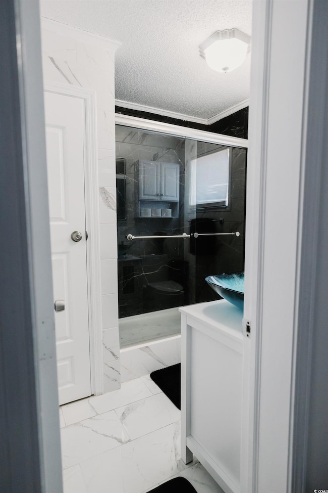Full bath with light marble finish flooring, a textured ceiling, vanity, and a marble finish shower