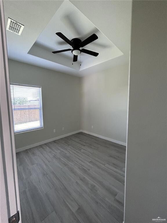 Empty room featuring a tray ceiling, wood finished floors, baseboards, and ceiling fan