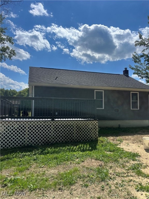 View of side of property featuring a wooden deck, a chimney, and a shingled roof