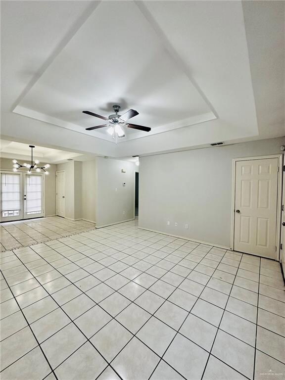 Unfurnished room featuring light tile patterned floors, ceiling fan with notable chandelier, and a tray ceiling