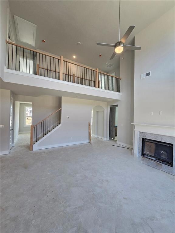 Two-story family room  with a high ceiling, a high end fireplace, ceiling fan, stairway, and arched walkways