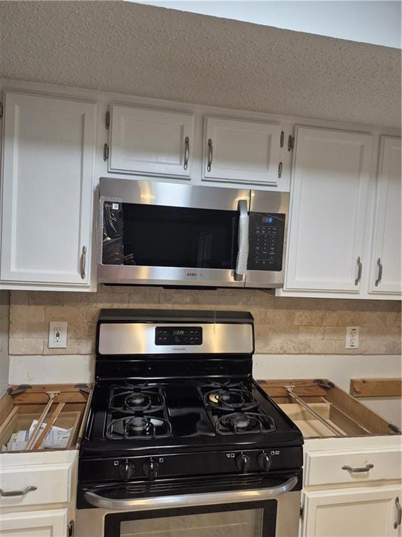 Kitchen featuring stainless steel appliances, decorative backsplash, white cabinets, and light countertops