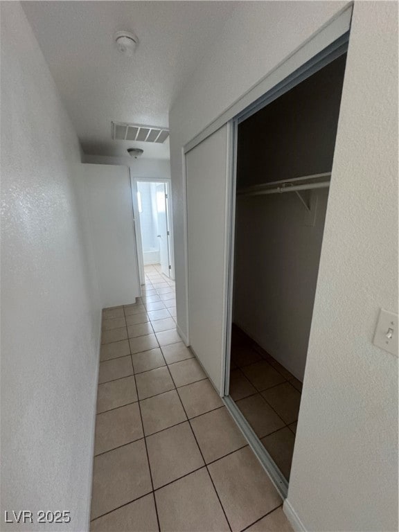 Hall with a textured wall, light tile patterned floors, and a textured ceiling