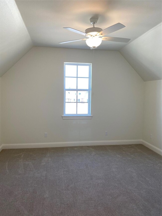 Bonus room with dark colored carpet, vaulted ceili