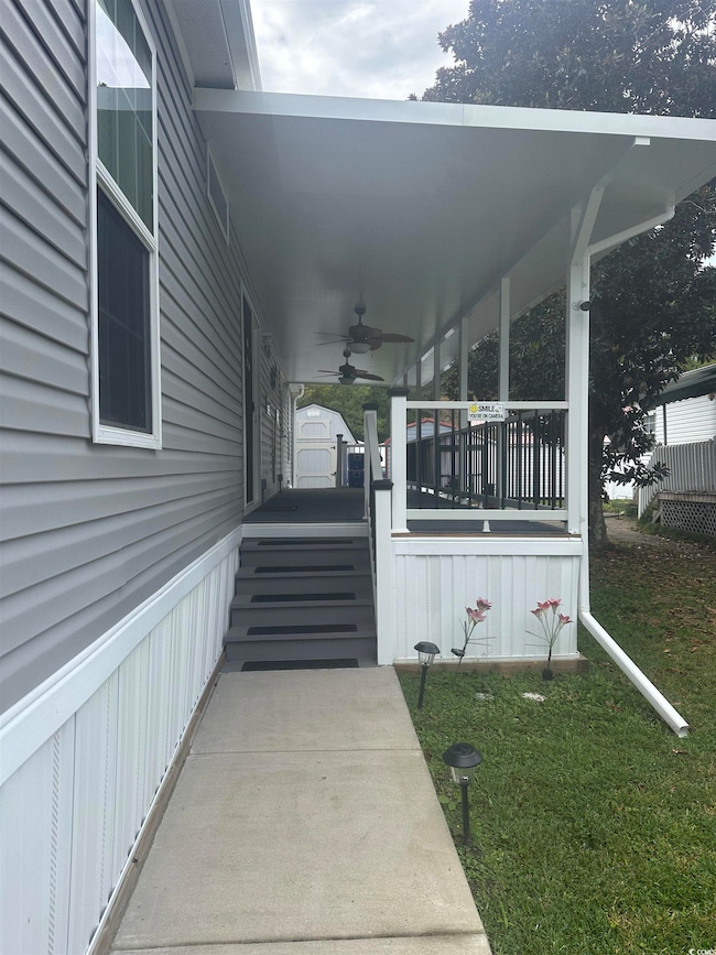 Entrance to property with a ceiling fan, a porch, and a yard
