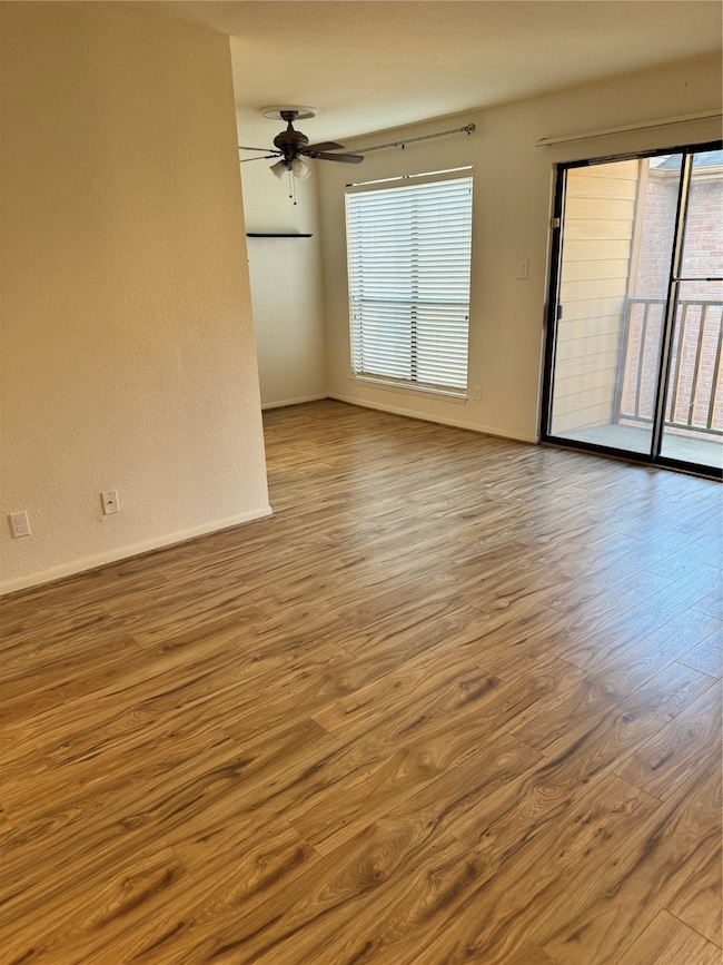 Bright, open-concept living area featuring beautiful wood-look floors, recessed lighting, and a cozy brick fireplace with a golden trim. Sliding glass doors open to a private balcony, filling the space with natural light.