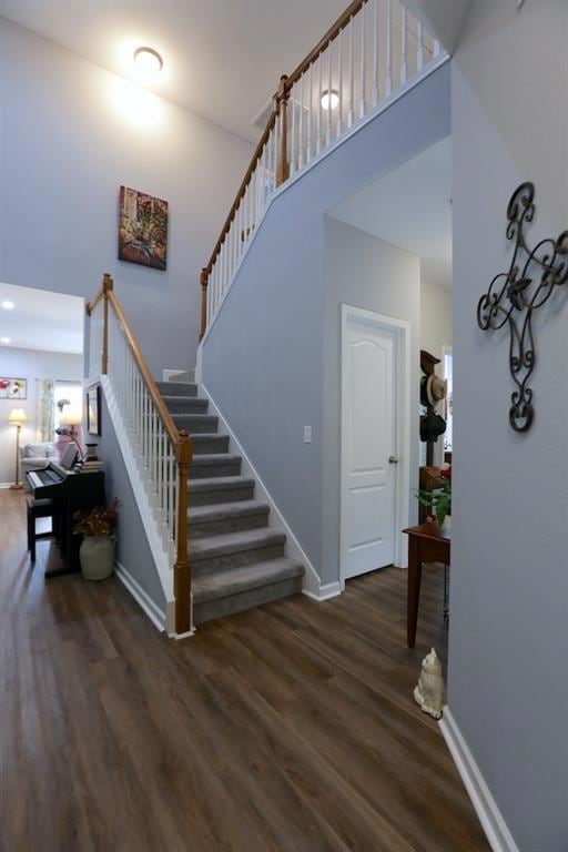 Staircase featuring a high ceiling, baseboards, and wood finished floors