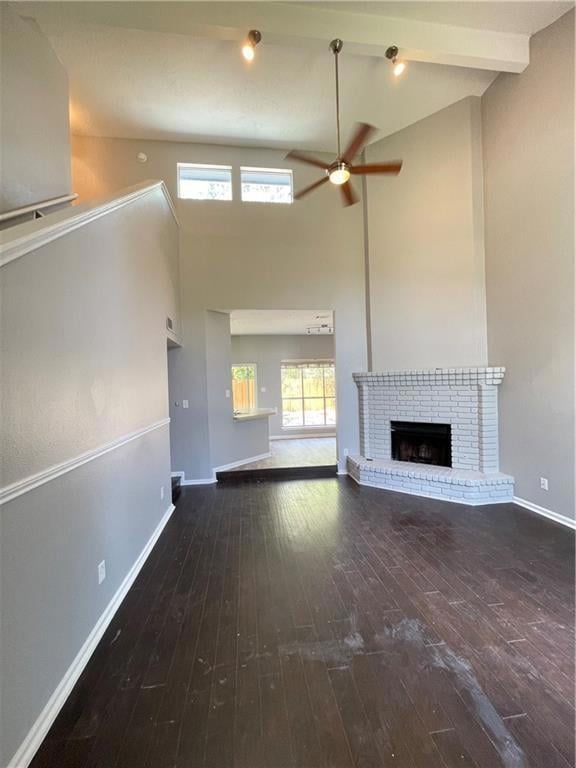 Unfurnished living room featuring a high ceiling, dark wood-type flooring, a fireplace, a ceiling fan, and beamed ceiling