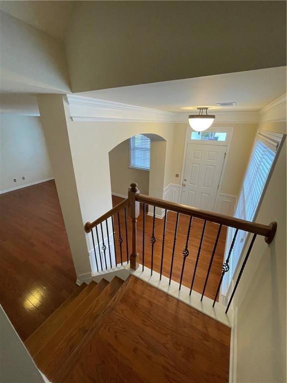 Staircase featuring ornamental molding, wood finished floors, arched walkways, and baseboards