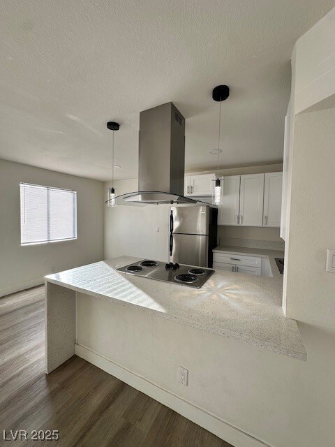 Kitchen featuring white cabinetry, decorative light fixtures, light stone counters, dark wood-style floors, and a peninsula