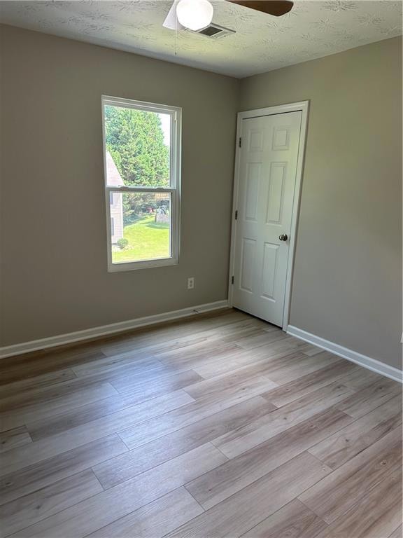 Empty room with a textured ceiling, a ceiling fan, and light wood finished floors