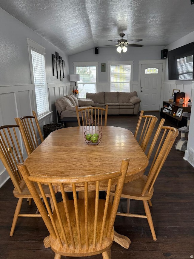 Dining room with a textured ceiling, wainscoting, a decorative wall, plenty of natural light, and dark wood-style floors