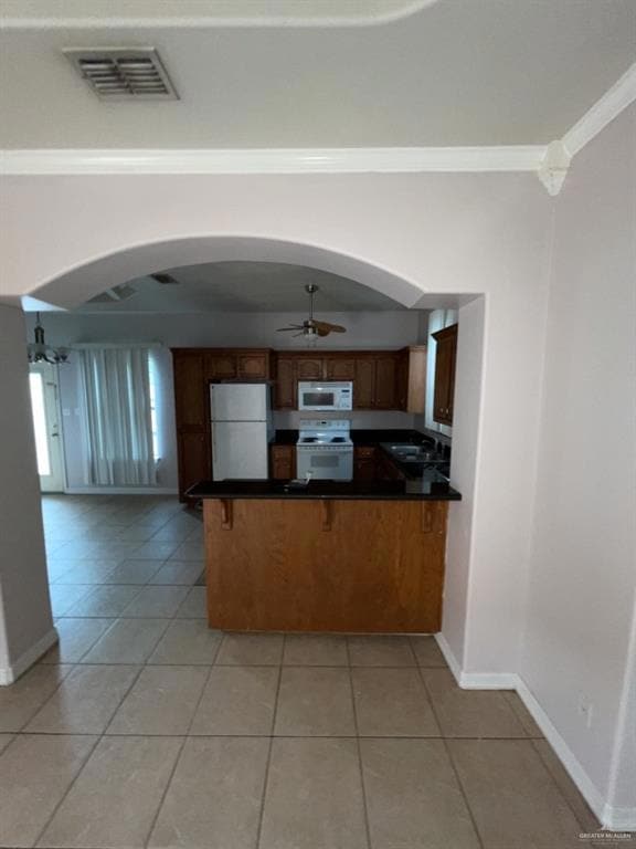 Kitchen featuring arched walkways, dark countertops, white appliances, ceiling fan, and light tile patterned floors