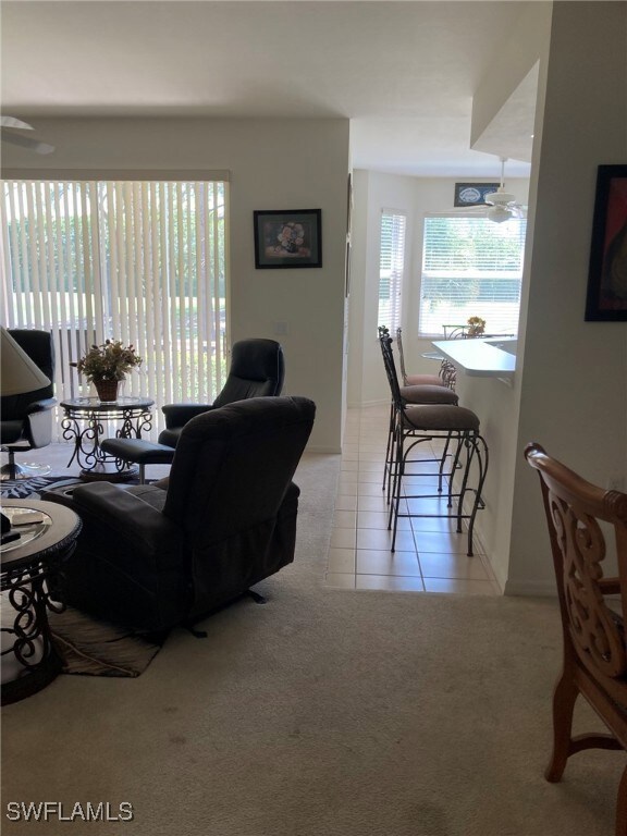 Living area with plenty of natural light, light carpet, light tile patterned floors, and a ceiling fan