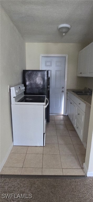 Kitchen featuring white electric stove, white cabinetry, light tile patterned floors, and a textured ceiling