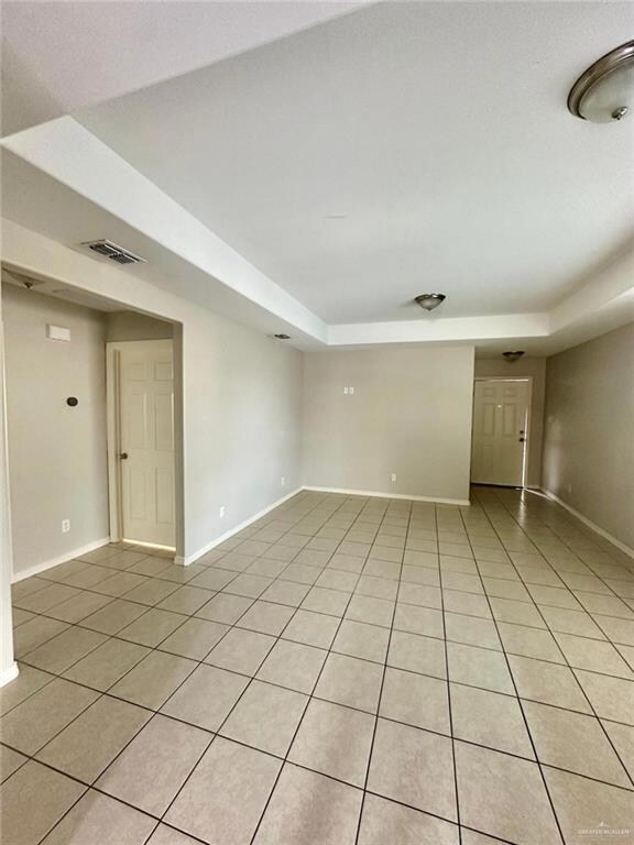Tiled empty room featuring a tray ceiling