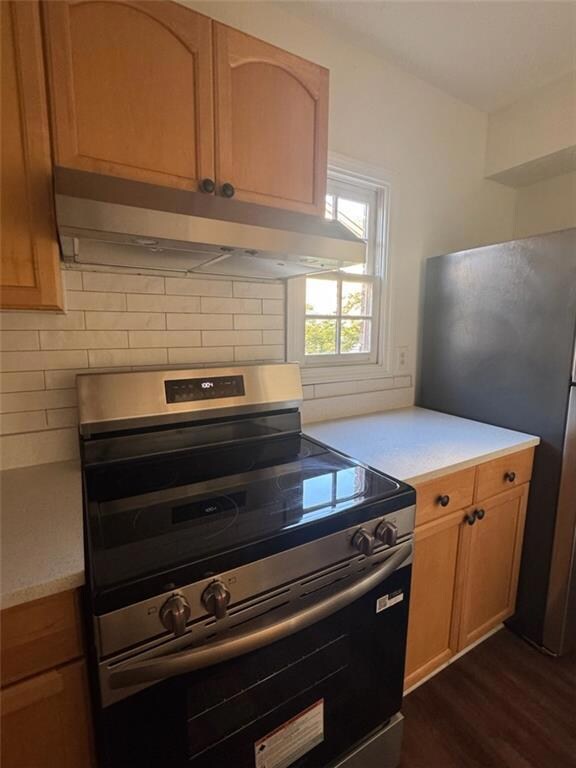 Kitchen with stainless steel appliances, under cabinet range hood, light countertops, tasteful backsplash, and dark wood-style floors